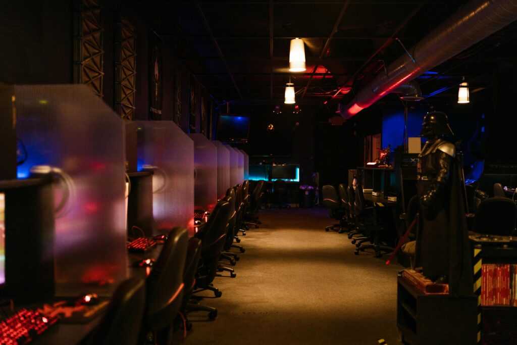 A dimly lit gaming arcade with neon lights and computers, creating a futuristic atmosphere.