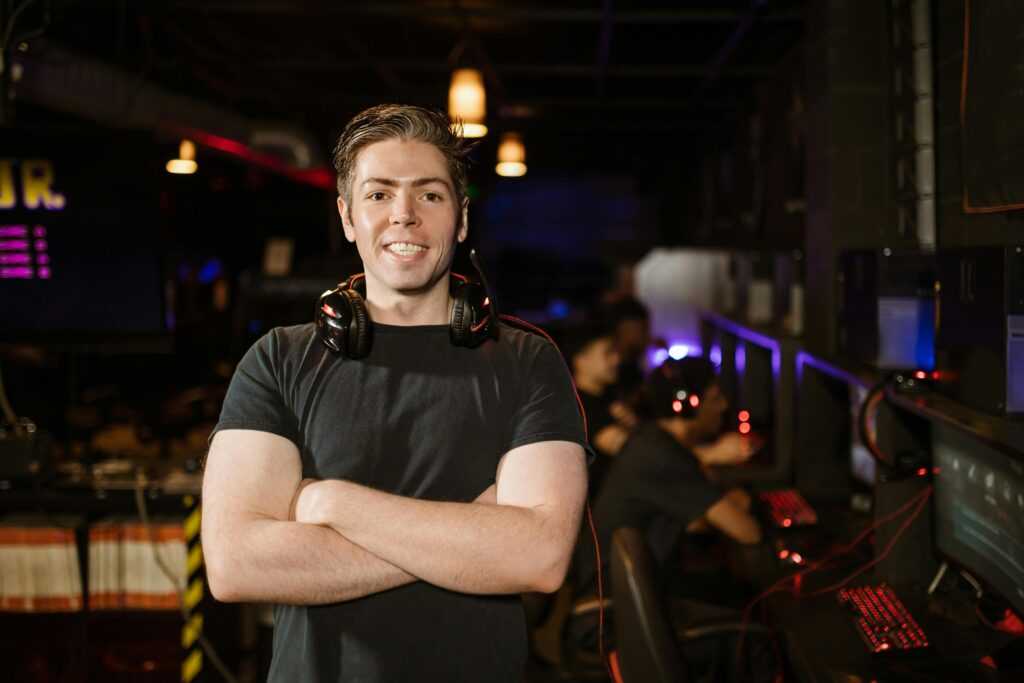 Smiling gamer standing with headphones in an illuminated gaming arena.