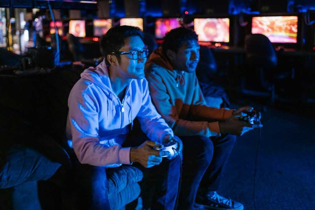 Two young men engaged in intense gaming with controllers under blue light indoors.