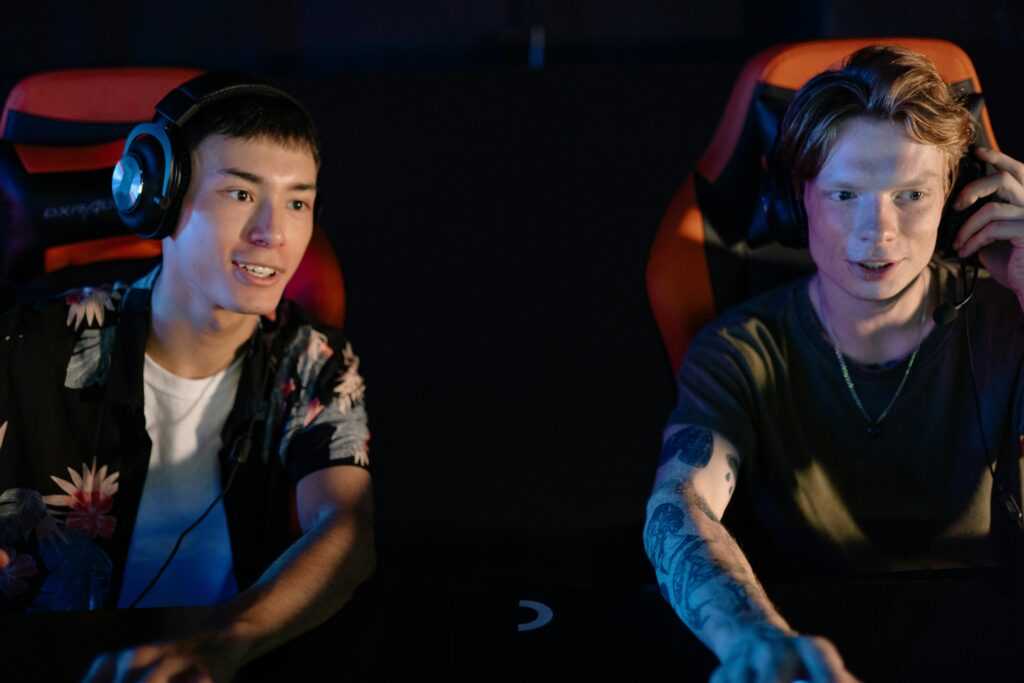Two young men focused on an intense gaming session in a dark room, participating in a team esports tournament.