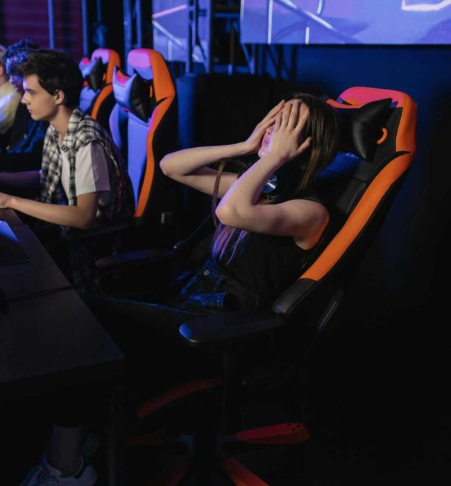 Woman covering eyes in gaming chair at esports event, expressing frustration after a loss.